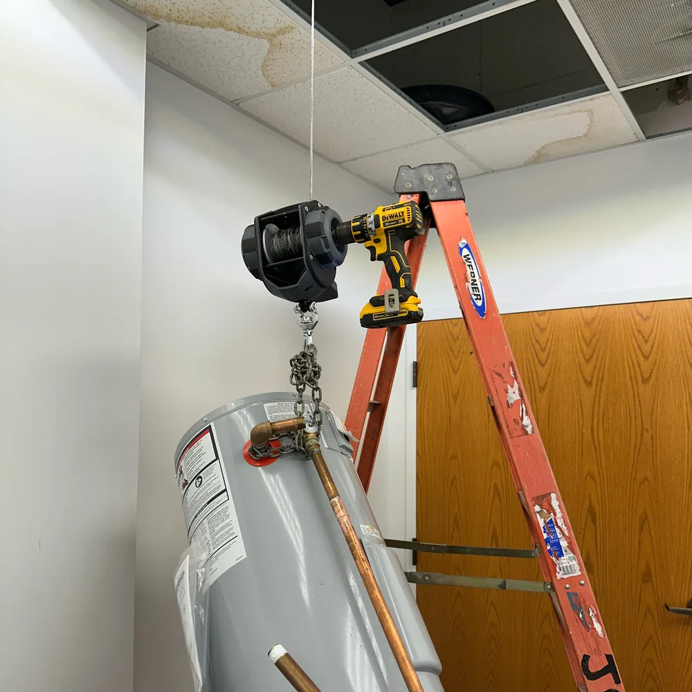 A Joel's Plumbing Service branded ladder beside a water heater being installed