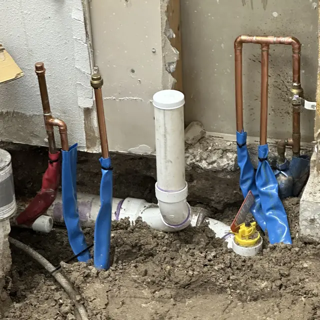 Copper supply risers and PVC drain rough-in at a wall penetration
