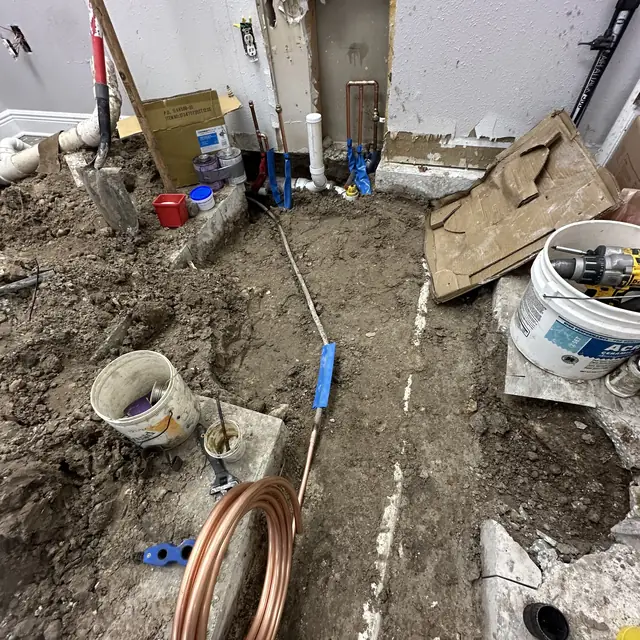 Coiled copper supply line beside a trenched drain run